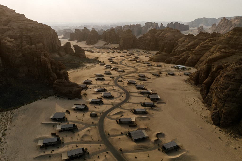 Aerial view of Our Habitas AlUla, low guest houses scattered across a sandy desert valley between sandstone cliffs